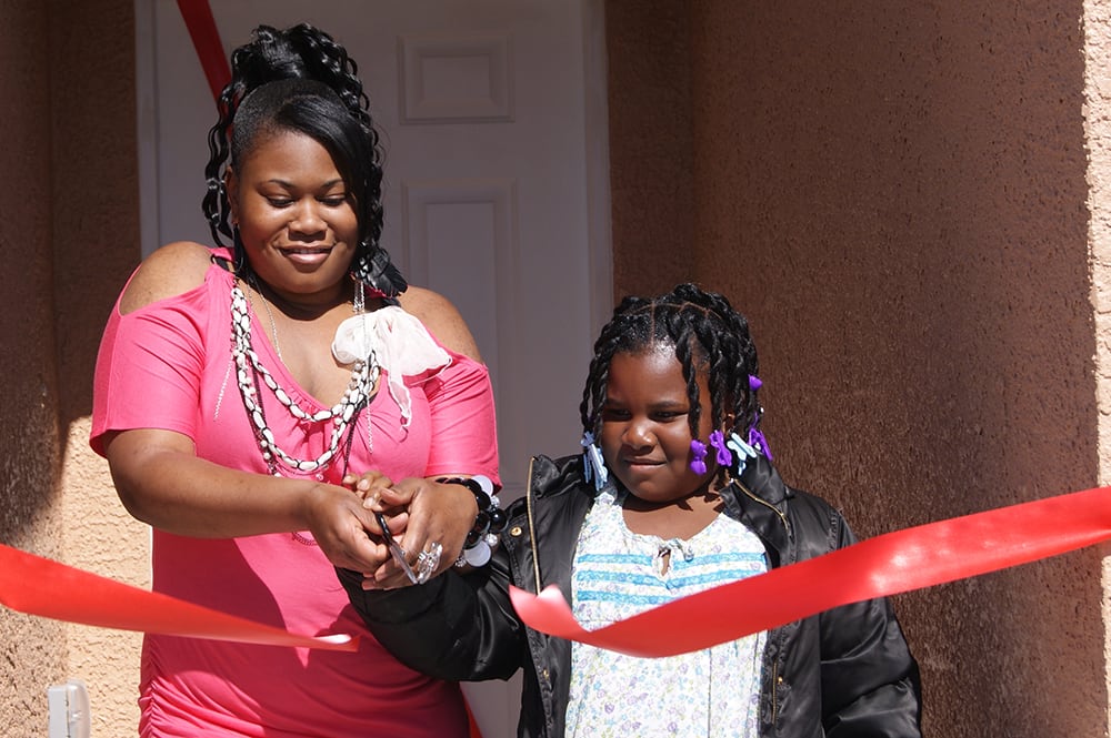 Adult and child cutting red ribbon to their new home