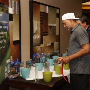 Man in a backwards cap places tickets into colored buckets at a table with gift baskets and a tournament sign.