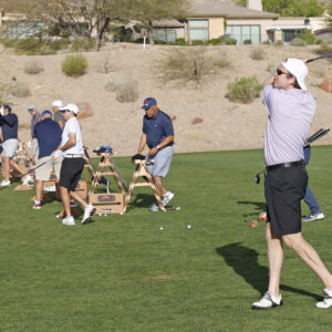 Golfers practice swings at a driving range on a sunny day, with golf balls and clubs on the grass.