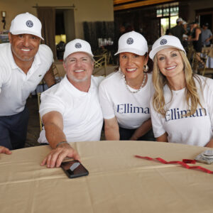 Four smiling adults in white shirts and hats pose around a table at an indoor event.