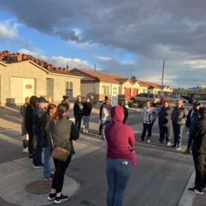 A group of people stands in a circle talking on a residential street at sunset.