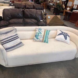 Curved white sofa with three decorative pillows, displayed in a furniture store.