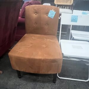Tan armless accent chair with button-tufted backrest, displayed in a secondhand furniture store.
