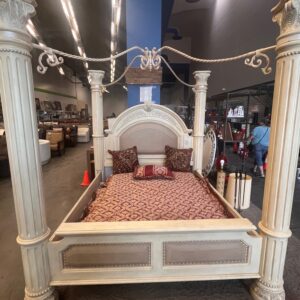 Ornate cream-colored canopy bed with decorative pillows, intricate carvings, and four tall corner posts.