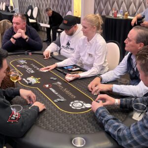 Five people play poker at a casino table, with a dealer in a white shirt handing out cards.