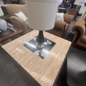 A beige marble-top side table with a lamp, surrounded by couches in a furniture store.