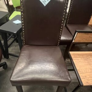 Brown faux leather chair with brass studs for sale, surrounded by other furniture in a store.