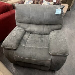 A gray, cushioned recliner chair on a showroom floor with sofas and price tags visible in the background.