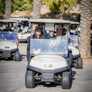 People riding golf carts on a sunny day, with palm trees and other golf carts in the background.