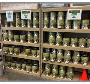 Shelves stocked with multiple cans of green paint, organized and labeled, with a single orange cone below.