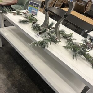 White table with holiday garland, two curved candle holders, and a sale sign, in a furniture store.