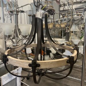 A rustic metal and wood chandelier hangs on display among other light fixtures in a store.