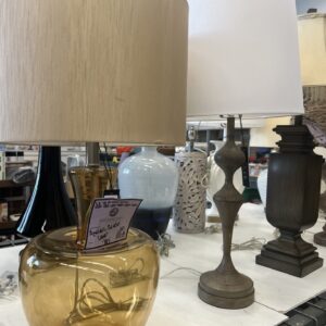 Two table lamps, one with an amber glass base and beige shade, the other with a wood base and white shade.