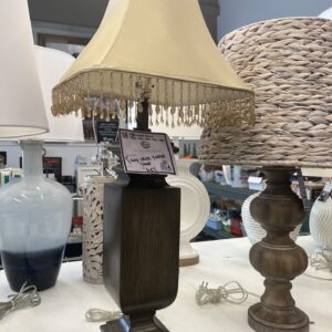 A brown table lamp with a beige fringed shade on display among other lamps in a store.