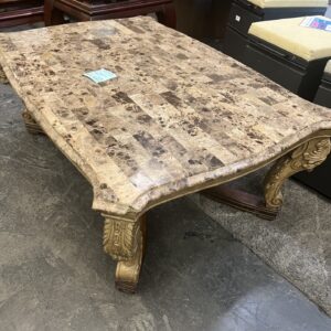 Rectangular marble-top coffee table with ornate carved wooden legs, set on a concrete floor in a store.