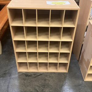 Wooden shelf unit with 20 square cubby holes, standing on a concrete floor in a furniture store.