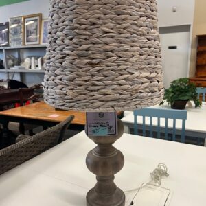 Table lamp with a woven wicker shade and wooden base displayed on a white table in a store.