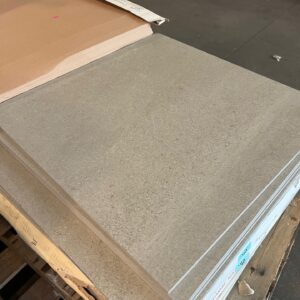 Stack of large, rectangular gray tiles placed on a wooden pallet in a warehouse setting.