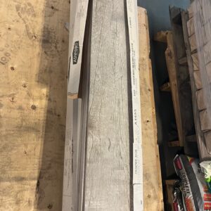A box of gray wood-look floor tiles sits on a wooden pallet in a warehouse.