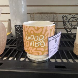 A mug with an orange wavy pattern and GOOD VIBES text sits on a black shelf among other decor items.