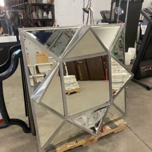 A geometric, multi-paneled mirror with triangular sections stands in a warehouse setting.
