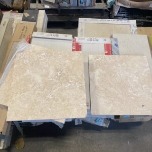 Two beige stone tiles on top of stacked boxes and various construction materials in a warehouse.