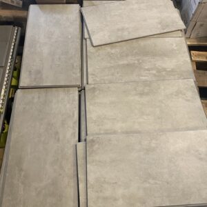 Stacks of large, rectangular gray floor tiles arranged on a pallet in a warehouse setting.