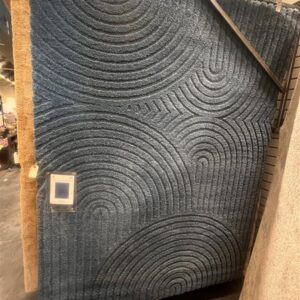 Blue rug with raised, curved line patterns displayed vertically in a store setting.