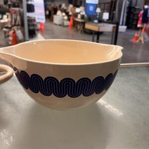 Cream-colored mixing bowl with blue wavy pattern on the side, displayed on a glass surface indoors.