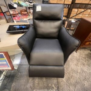 A black leather armchair is displayed in a store, surrounded by shelves, boxes, and various items.