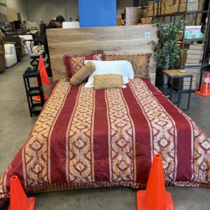 A bed with red patterned bedding is displayed in a store, surrounded by orange traffic cones.