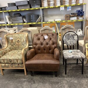Three assorted chairs in front of shelves with bins and boxes at a thrift store or warehouse.