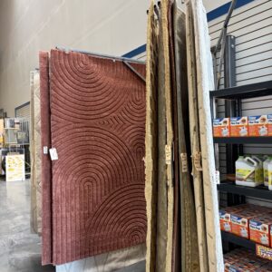 Several large rugs in various colors and patterns are displayed on racks in a store aisle.