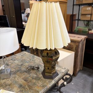 Table lamp with a pleated cream lampshade on a marble-top table in a furniture store.