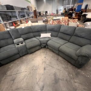 Large gray sectional sofa with cup holders, displayed in a warehouse with various other furniture items.