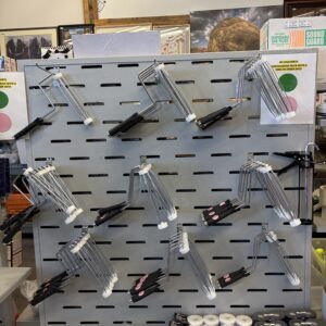 Paint roller handles are displayed on a pegboard wall in a hardware store, with other supplies below.