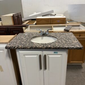 White bathroom vanity with granite countertop and sink, surrounded by various cabinet pieces.
