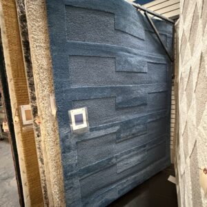 Blue area rug with a modern geometric pattern displayed among other rugs in a store showroom.