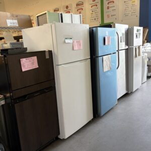 A row of five used refrigerators in various colors and styles displayed in a store.