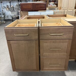 Two wooden kitchen cabinets with gold handles displayed in a showroom with other cabinets in the background.