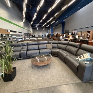 A large black sectional sofa and a round glass coffee table on a rug in a spacious furniture showroom.