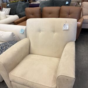 A beige upholstered armchair with a tag, displayed among other sofas in a furniture store.