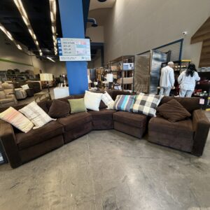 Large brown sectional sofa with assorted throw pillows on display in a spacious furniture store.