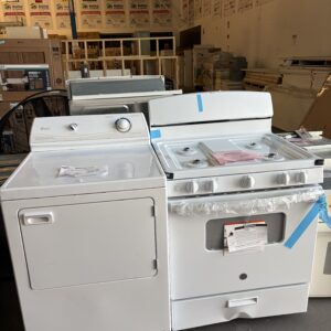 A white dryer and a white stove side by side in a store with building materials in the background.