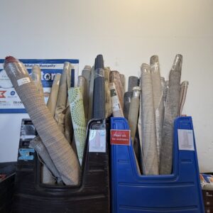 Several rolled-up rugs wrapped in plastic standing upright in blue and brown bins against a wall.