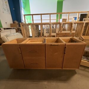 Wooden kitchen cabinets displayed in a store with other building materials in the background.