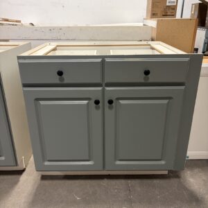Gray cabinet with two drawers and two doors, displayed in a warehouse setting with boxes in the background.