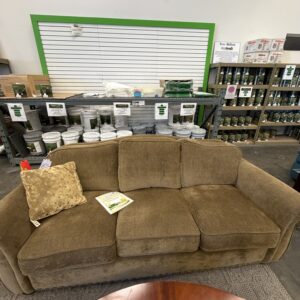 Brown sofa with a pillow and open book, in front of shelves with paint cans in a store setting.