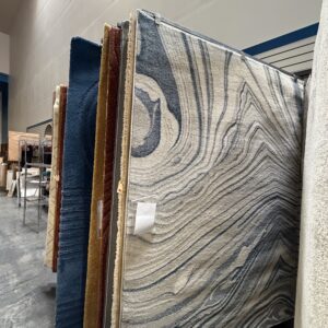 Large patterned rugs displayed upright in a store, with various colors and designs visible along the aisle.