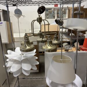 Various light fixtures and lampshades displayed on a metal shelving unit in a warehouse setting.